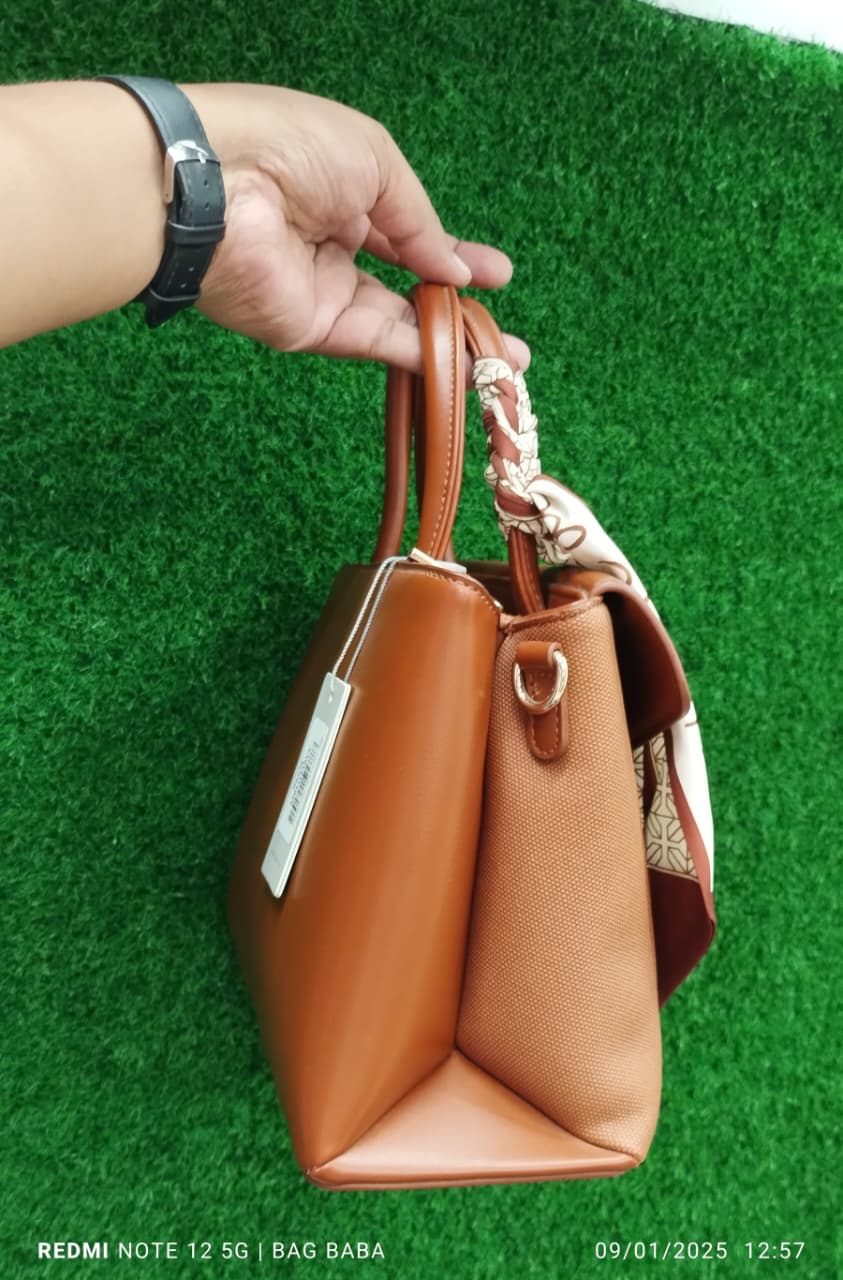 Brown handbag held by a hand against a green grass background