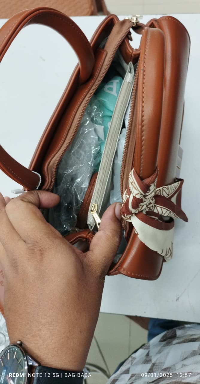 Brown handbag with decorative bow held by a hand on a white background